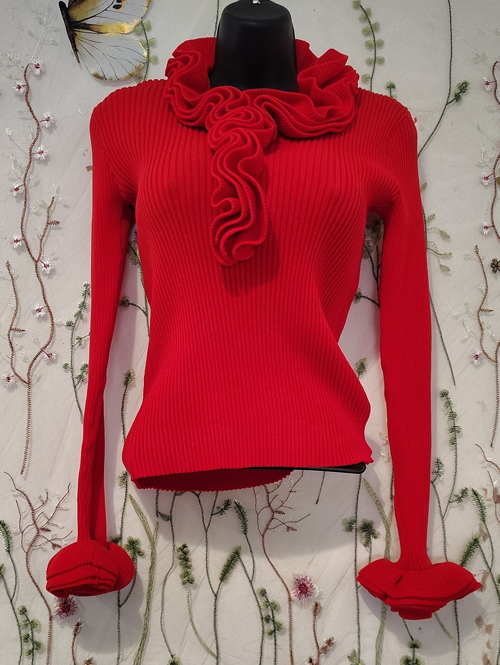 This vibrant ribbed knit sweater features a unique, dramatic cascading ruffles